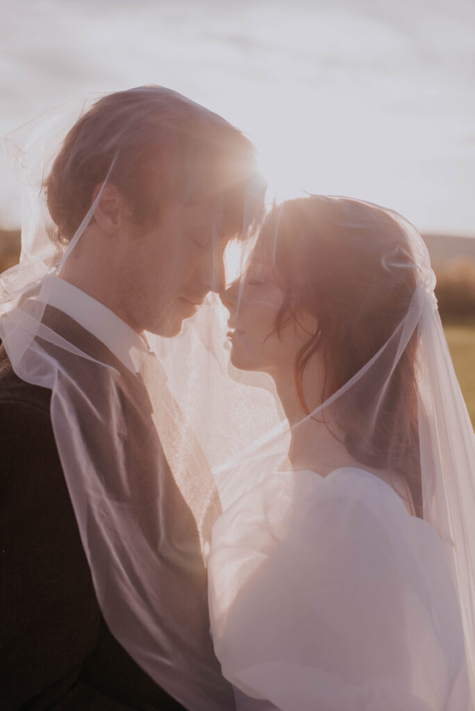 romantic photo of bride and groom posed under veil at sunset