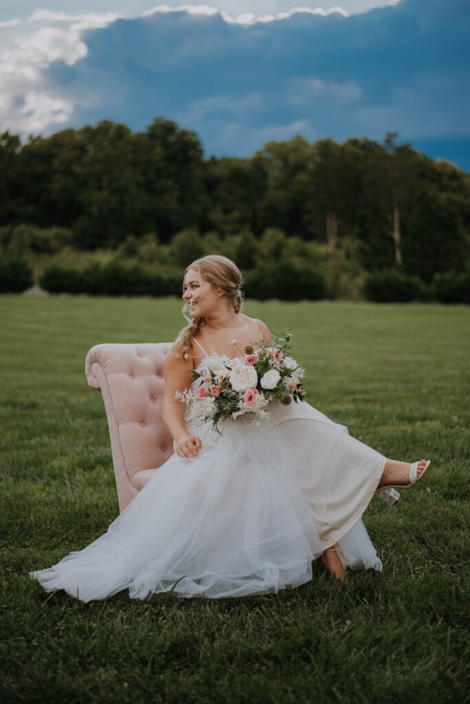 bride sits on tufted pink chair on the lawn